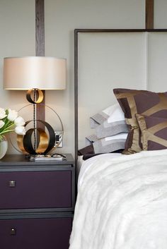 a bed with white sheets and pillows next to a night stand with flowers on it