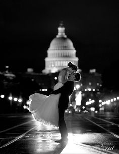 a bride and groom dance in front of the capital building at night during their wedding reception