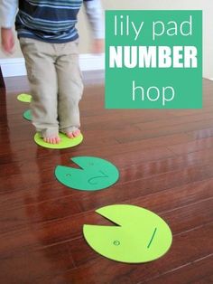 a young child standing on top of a wooden floor next to a green sign that says lily pad number hop