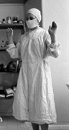 a woman in a surgical gown is standing with her hands up to the ceiling and she has one hand raised