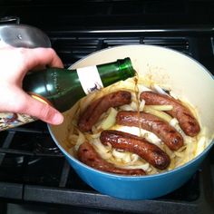 someone is pouring wine into a pot full of onions and sausages on the stove