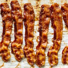 bacon strips are lined up on a sheet of waxy baking paper, ready to be cooked