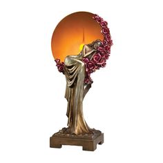 a golden statue with roses around it holding a lit candle in its hand and sitting on a wooden base