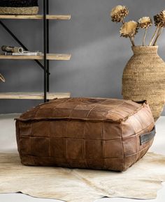 a brown leather ottoman sitting on top of a rug next to a vase filled with dried flowers