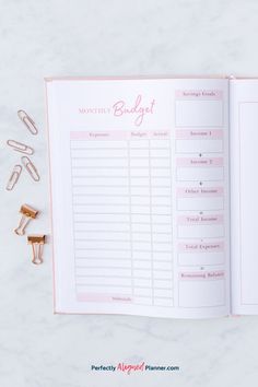 an open planner with pink writing on it and some gold clips next to it that says month's budget