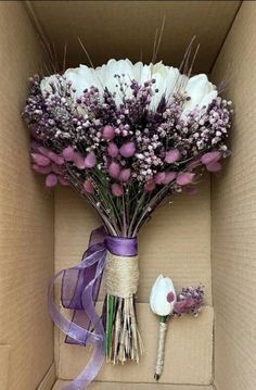 a bouquet of flowers in a box with a purple ribbon tied around it and an artificial flower