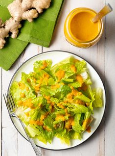 a white plate topped with lettuce next to a glass of orange juice and ginger