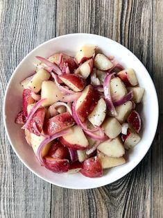 a white bowl filled with potatoes and onions on top of a wooden table next to a fork