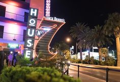 people are standing in front of a building at night with palm trees and neon lights