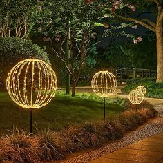 three lighted orbs in the grass near trees and bushes at night with lights on them