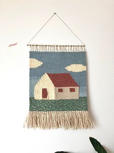 a tapestry hanging on the wall with a house and clouds in the sky above it