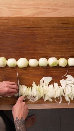 a person cutting onions on top of a wooden table with a pair of knifes