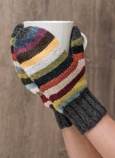 a woman's hand holding a coffee cup with multi - colored knitted mitts