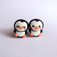 two little penguins sitting next to each other on top of a white surface with one penguin looking at the camera