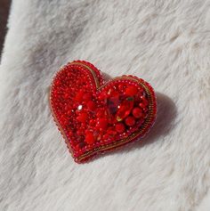 a red heart shaped brooch sitting on top of a white blanket