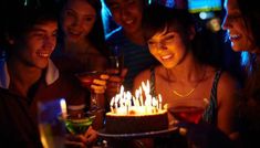 a group of people standing around a cake with lit candles