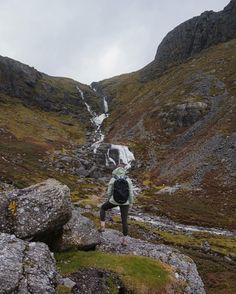 a person with a backpack is standing on some rocks and looking up at a waterfall