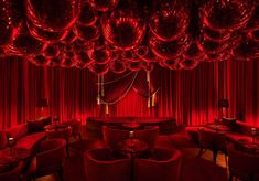 a room filled with lots of red balloons hanging from the ceiling and round tables in front of it