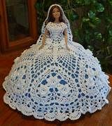 a crocheted doll in a white dress on a wooden table with greenery