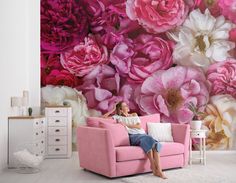 a woman sitting on a pink couch in front of a floral wall mural