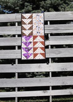 a quilted wall hanging on the side of a wooden fence with trees in the background