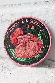 a patch with the words slowly but surely written on it and a large pink flower