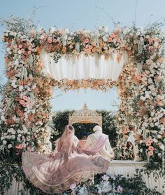 the bride and groom are sitting in front of an elaborate floral arch with flowers on it