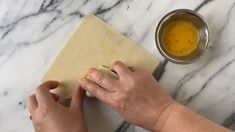 a person is peeling an onion on a cutting board next to a bowl of mustard