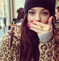 a woman wearing a leopard print coat and hat with her hand on her mouth in front of her face