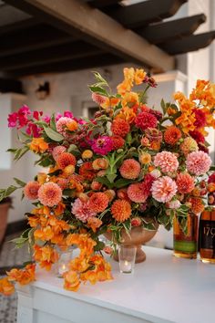 an arrangement of flowers in vases sitting on a white counter top next to two bottles