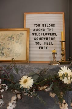 two framed pictures and some flowers on a mantle