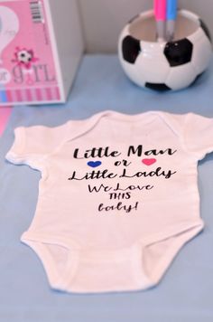 a baby's bodysuit with writing on it sitting next to a soccer ball