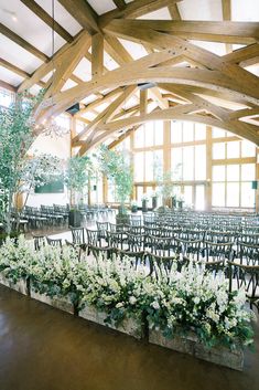 rows of chairs with flowers on them in a large room filled with windows and wooden beams