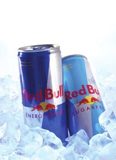 two cans of red bull energy drink sitting on top of some ice cubes in the snow