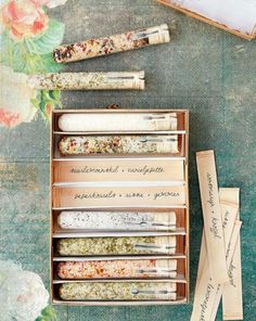 an assortment of herbs in wooden boxes on a table with flowers and writing utensils