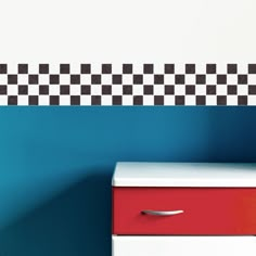 a red and white dresser next to a blue wall with black and white checkered border