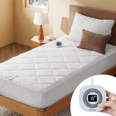 a person holding an alarm clock in front of a bed with white sheets and pillows