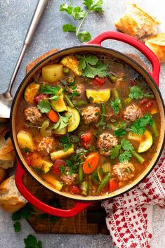 a red pot filled with meat and vegetable soup on top of a wooden cutting board