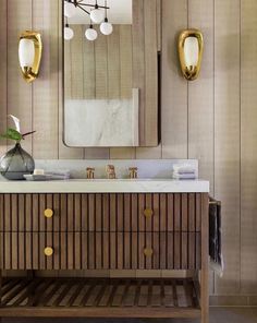 a bathroom vanity with marble counter top and gold accents on the mirror, along with two brass sconces