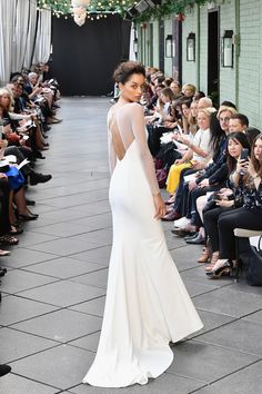 a woman in a white dress walking down a runway with people watching her on the phone