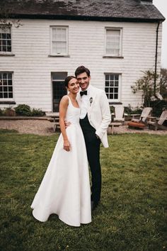 a bride and groom standing in front of a white house on their wedding day, posing for the camera