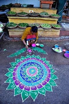 a woman is drawing on the ground in front of her shop with colored chalks