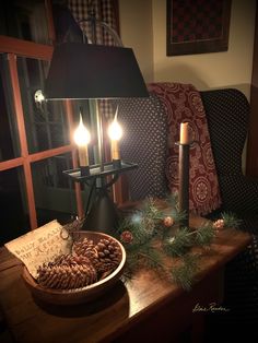 two candles are lit on a table with pine cones