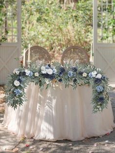 a table with flowers and greenery is set up for an outdoor wedding reception in the shade