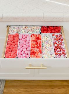 a drawer filled with different colored candies on top of a wooden floor next to a counter