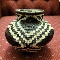 a black and white vase sitting on top of a red tablecloth covered floor next to a couch