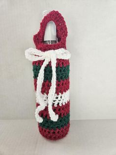 a crocheted red and green bottle cover with a white ribbon on the top