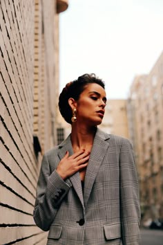 a woman standing next to a brick wall wearing a blazer and pants with her hands on her chest