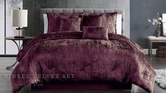 a bed with purple comforter and pillows in a room next to a lamp on a table