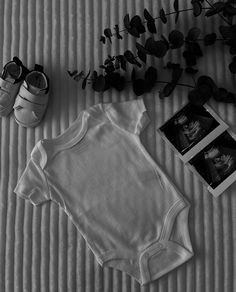 an infant's bodysuit, shoes and plant are on the bed next to it